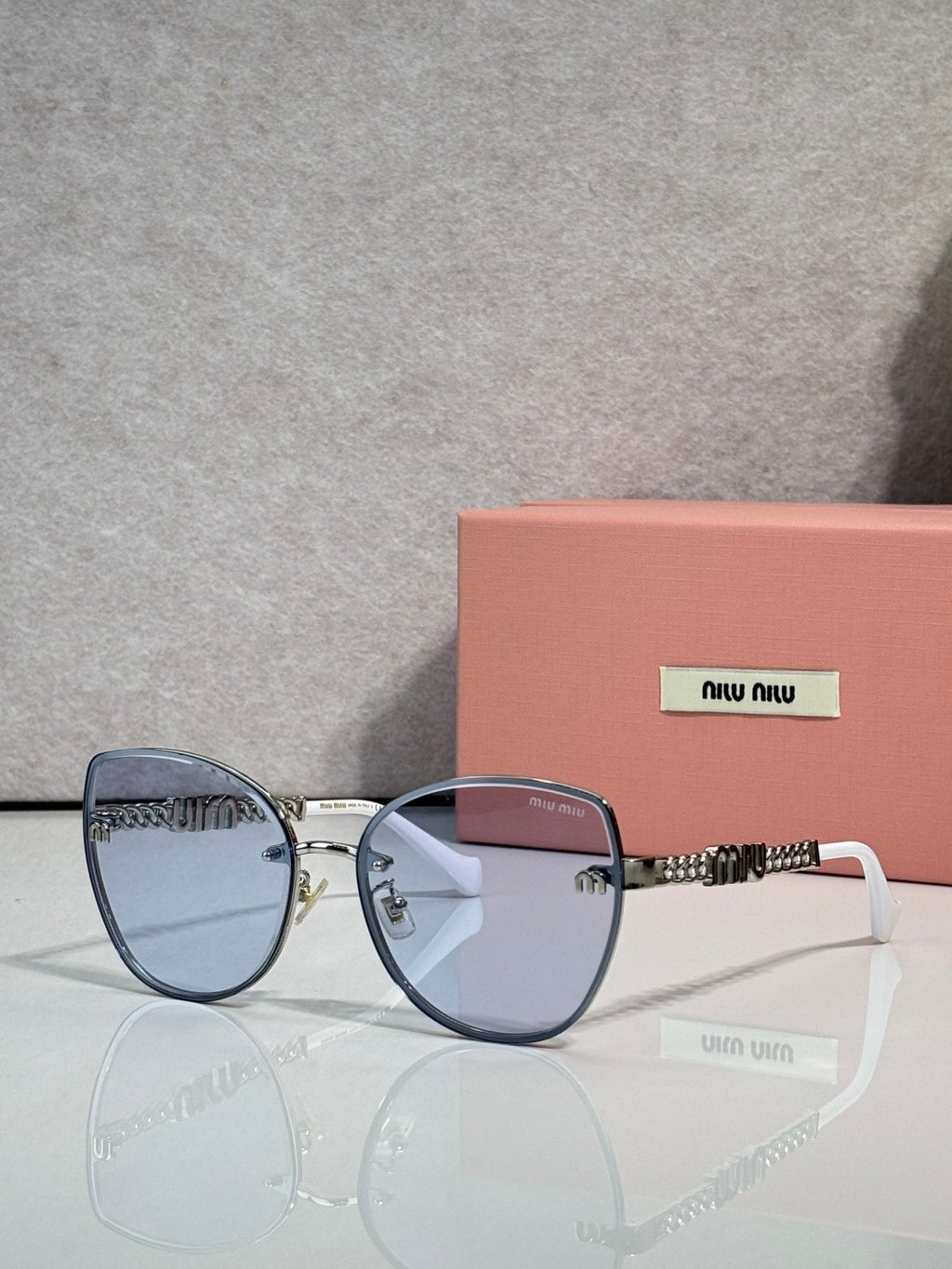 MiuMiu round sunglasses with blue frame, light blue lenses, and gold chain temple detail.