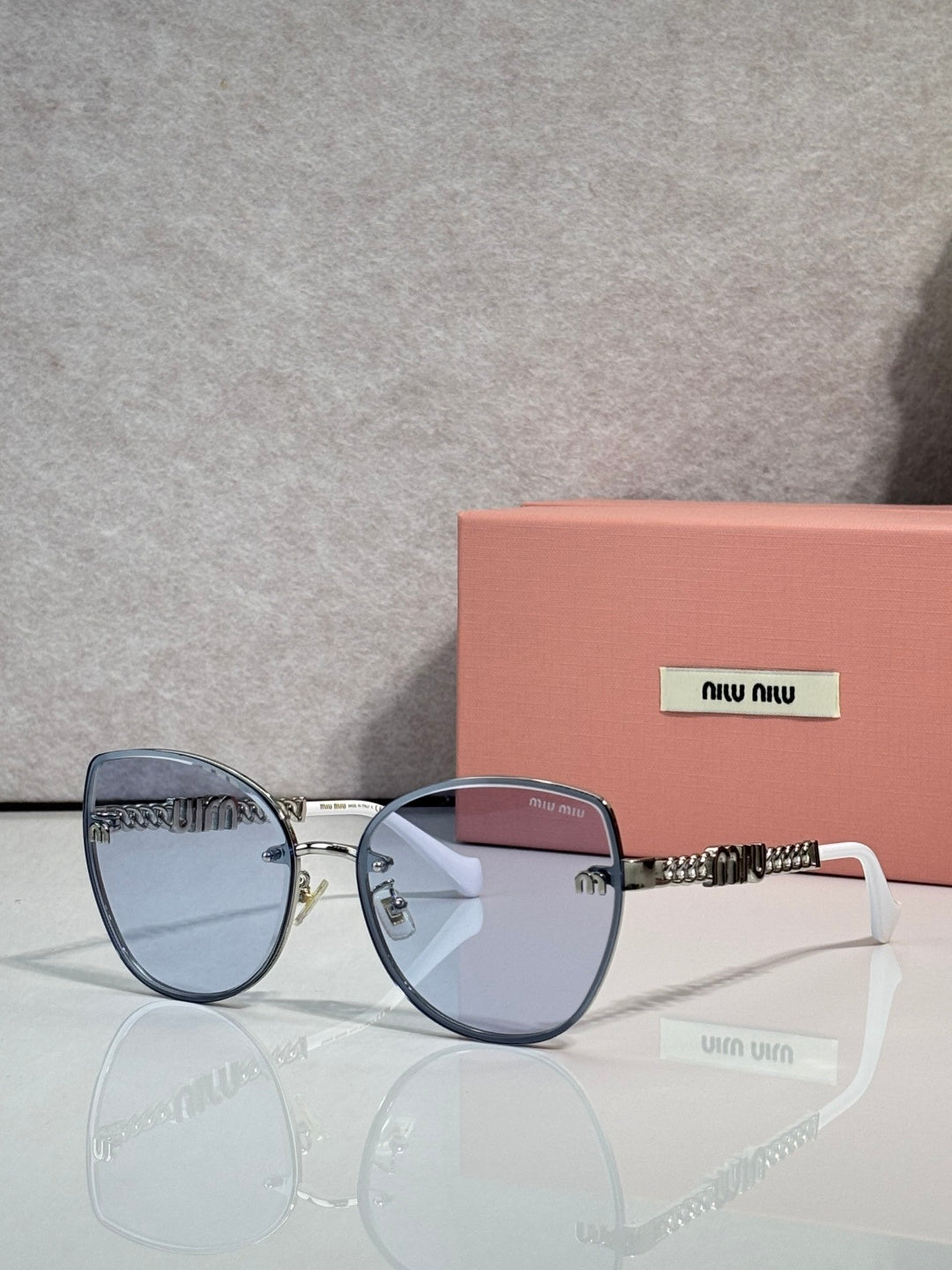 MiuMiu round sunglasses with blue frame, light blue lenses, and gold chain temple detail.