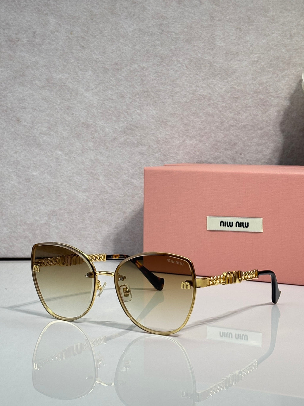 MiuMiu round sunglasses with gold frame, brown gradient lenses, and gold chain detail.