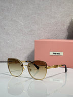 MiuMiu round sunglasses with gold frame, brown gradient lenses, and gold chain detail.