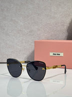 MiuMiu round sunglasses with black frame, dark lenses, and gold chain on the temple.