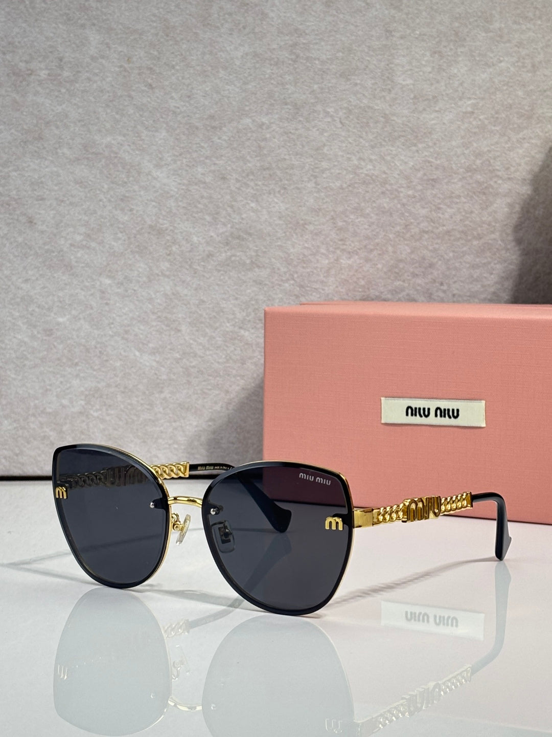 MiuMiu round sunglasses with black frame, dark lenses, and gold chain on the temple.