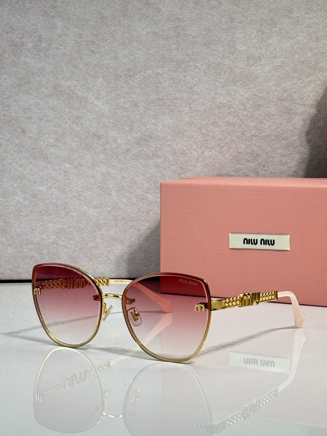 MiuMiu round sunglasses with gold frame, pink gradient lenses, and chain detail temples.