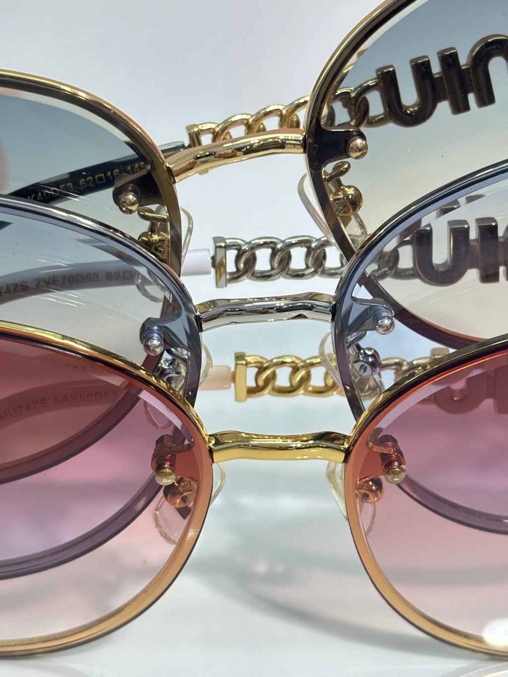 MiuMiu sunglasses close-up: overlapping round frames with engraved temples and chain detail.