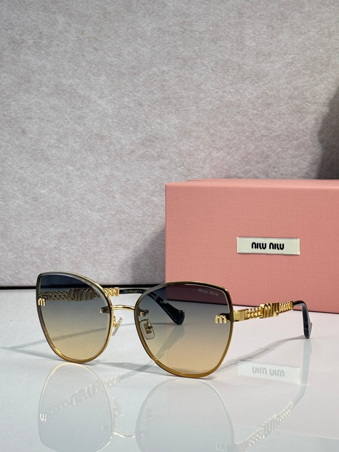 MiuMiu round sunglasses with gold-trim frame, gradient lenses, and chain temple detail.