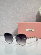 MiuMiu round sunglasses with black frame, dark lenses, and silver chain temple detail.