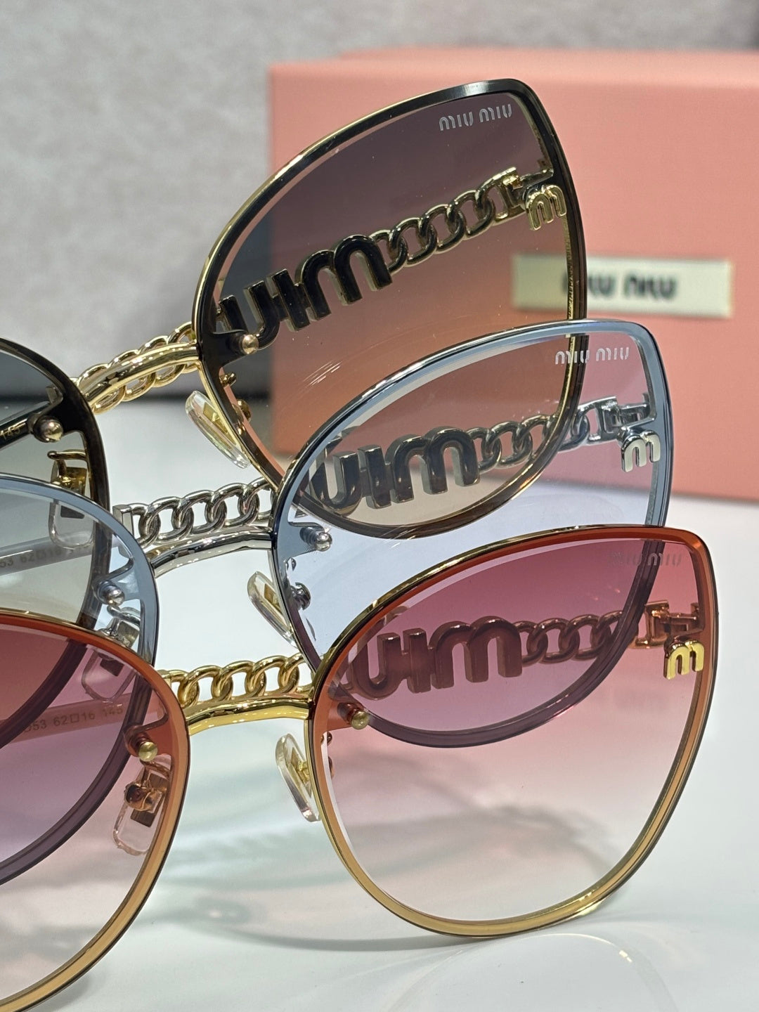 MiuMiu sunglasses close-up: engraved temple with chain detail and overlapping lens fronts.