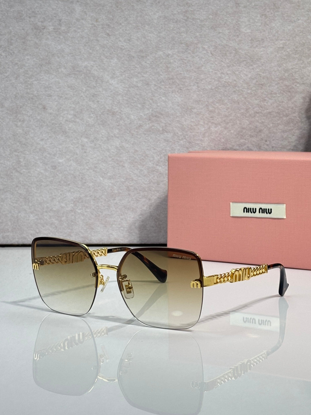 Sunglasses with gradient amber lenses, gold frame and chain temples, black ear tips.
