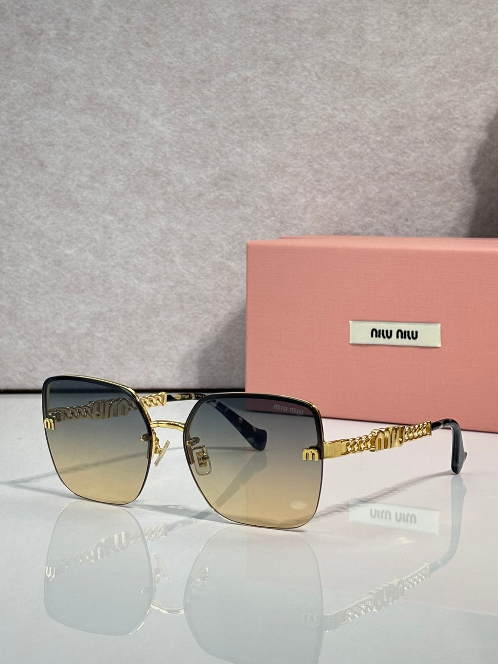 Sunglasses with amber-tinted lenses, gold frame and chain temples, black ear tips.
