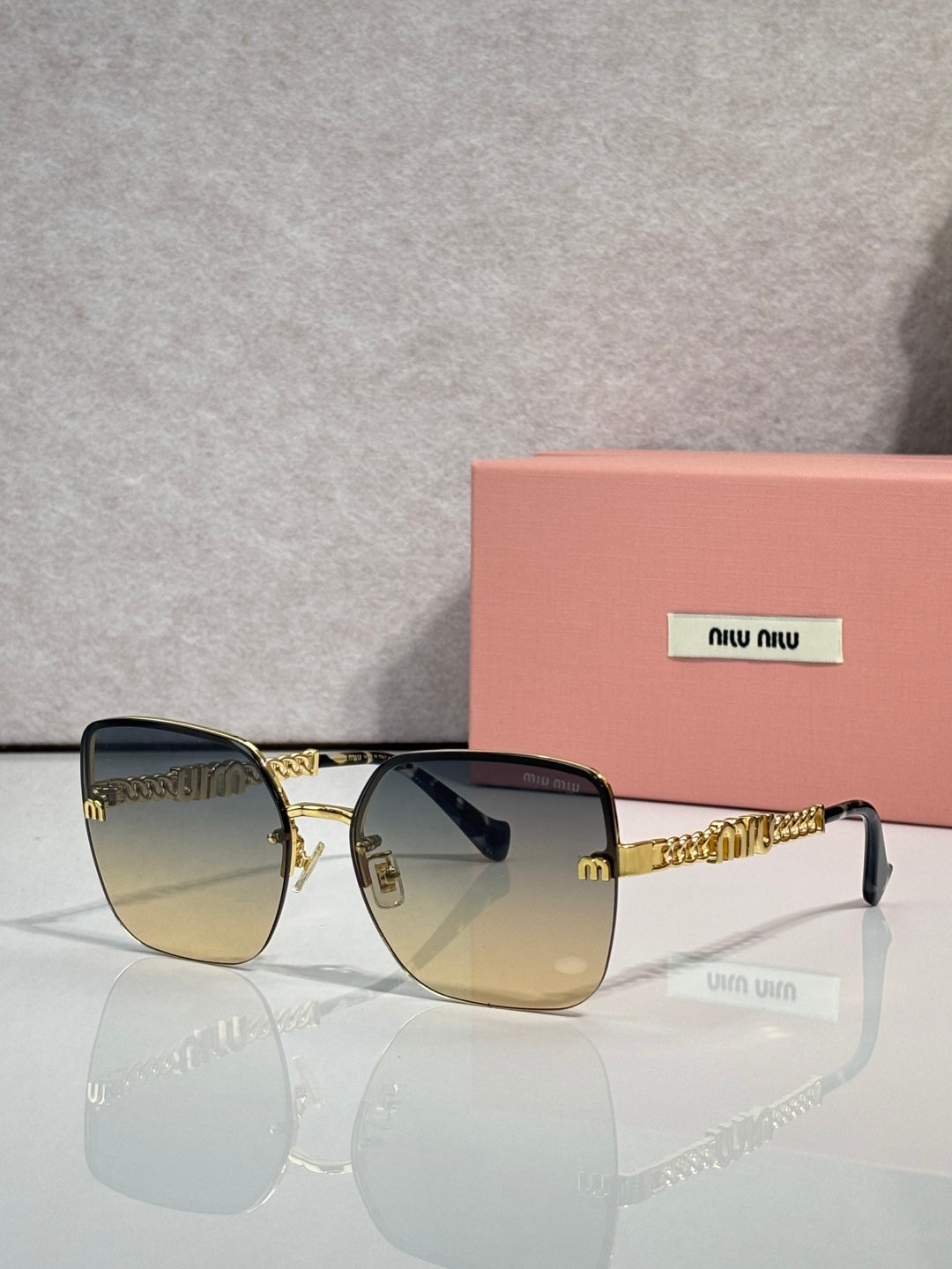 Sunglasses with amber-tinted lenses, gold frame and chain temples, black ear tips.