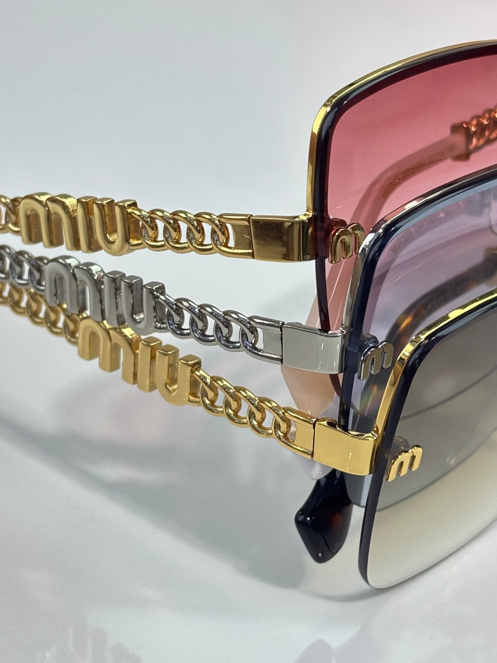 Sunglasses side view with gold chain temple, pink lenses, and gold-and-black frame.