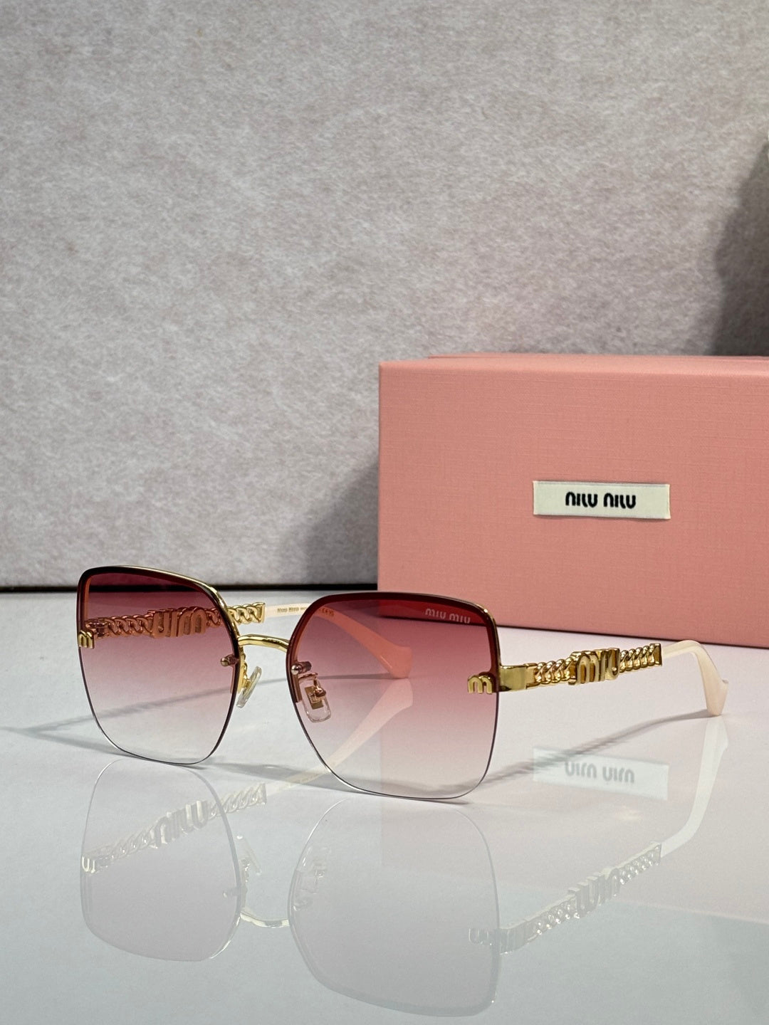 Sunglasses with pink-tinted lenses, gold frame and chain temples, dark ear tips.