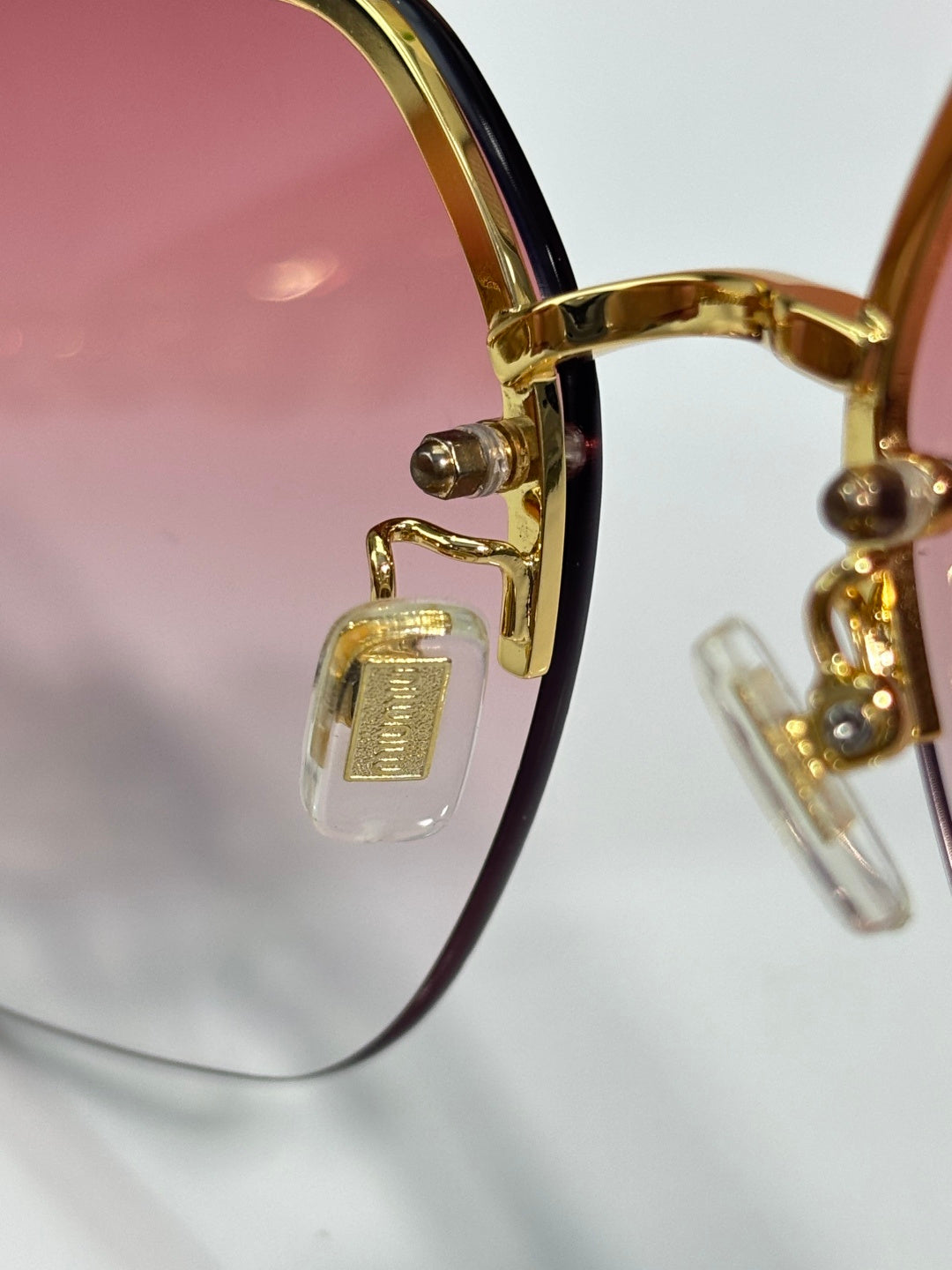Sunglasses close-up: gold hinge and chain detail with maroon inner frame.
