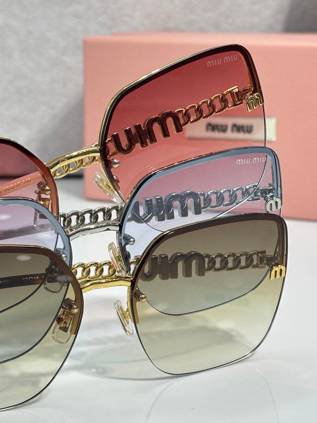 Sunglasses close-up: stacked gold-and-black temple lettering and pink lenses.