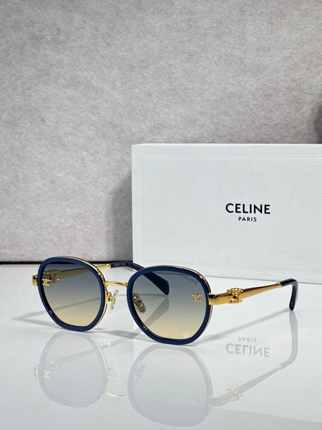 Round sunglasses with navy frame and gold-tone rims, light gradient lenses