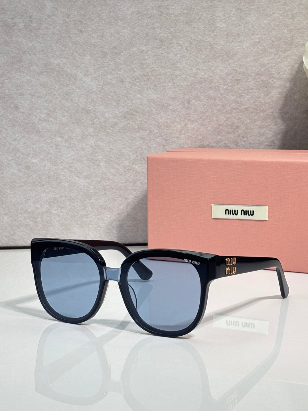 Sunglasses with dark frames and blue-tinted lenses, rounded shape with temple logo