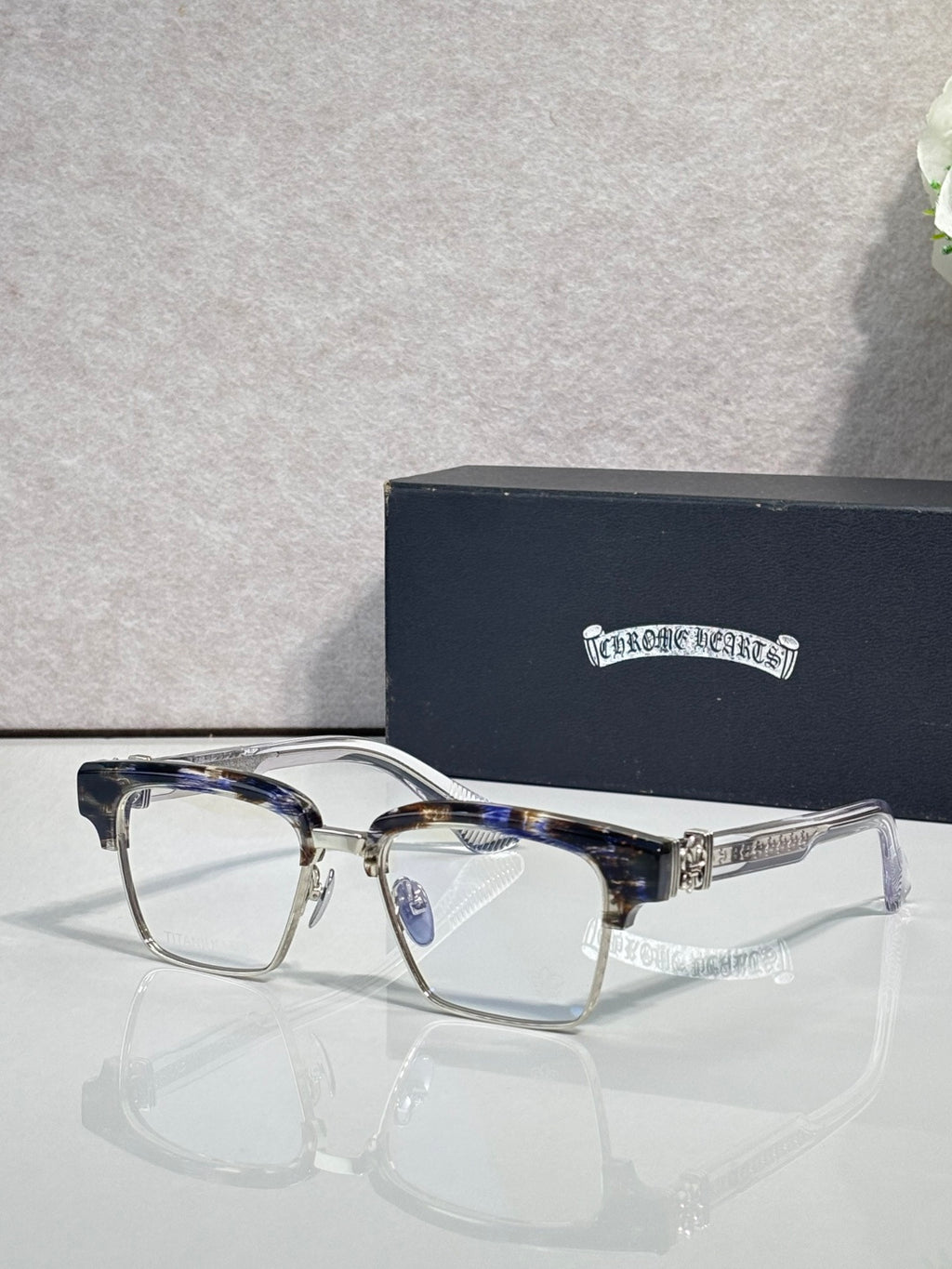 Patterned navy-and-silver eyeglass frames with square clear lenses and silver temple logo