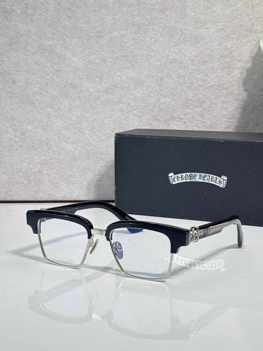 Black-and-silver eyeglass frames with square clear lenses and engraved temple logo