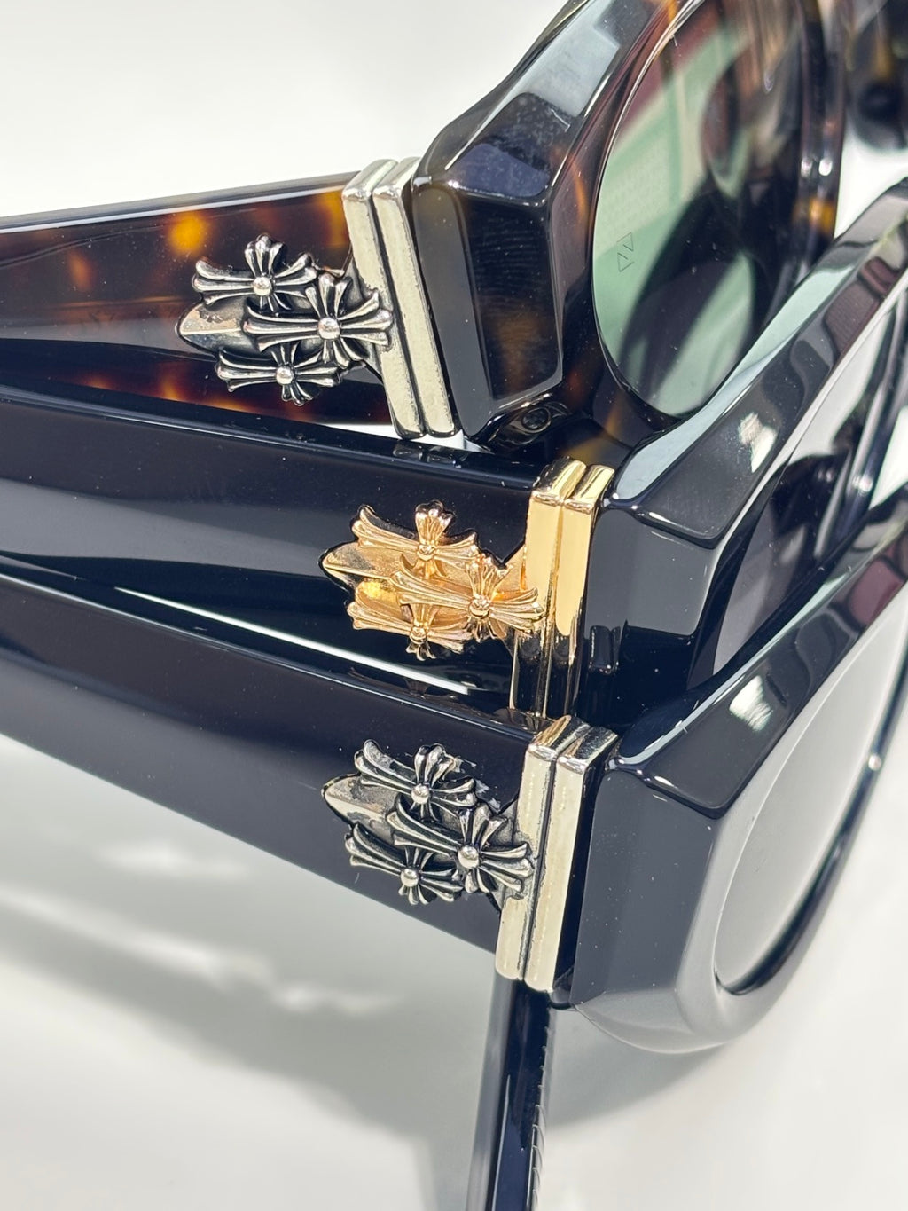 Close-up of glasses hinge with gold and silver floral-style emblems on a dark frame