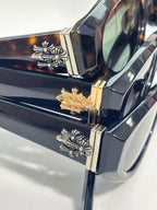 Close-up of glasses hinge with gold and silver floral-style emblems on a dark frame