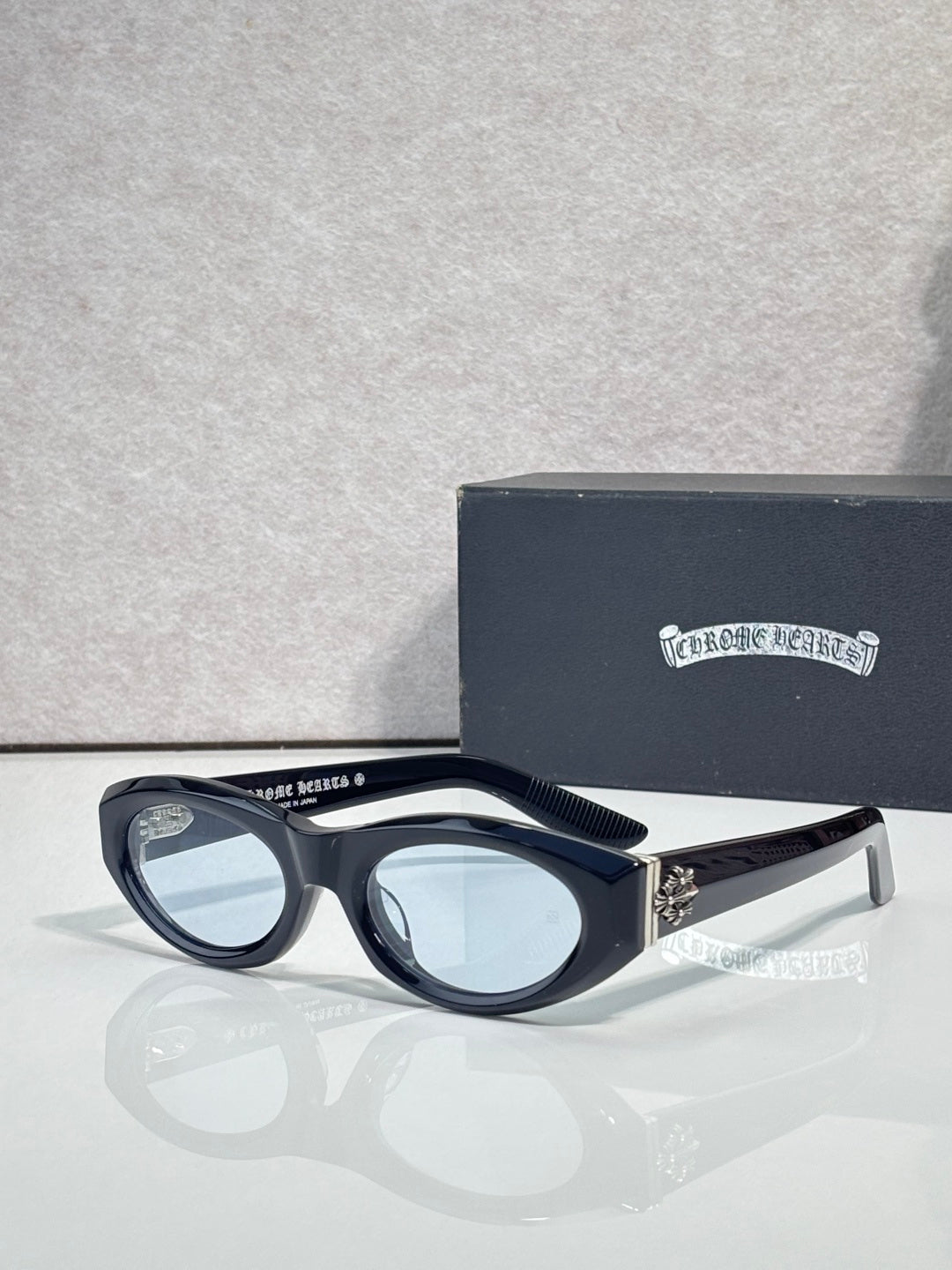 Cat-eye glasses with dark frame and tinted lenses, featuring a metallic side emblem