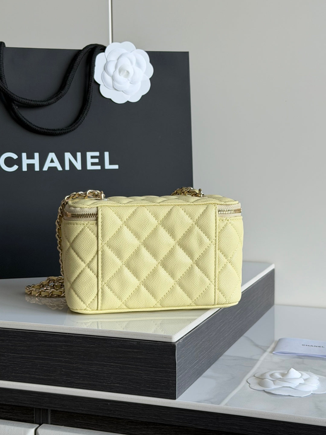 Chanel quilted mini crossbody bag with gold chain strap in pale yellow, side view on stand