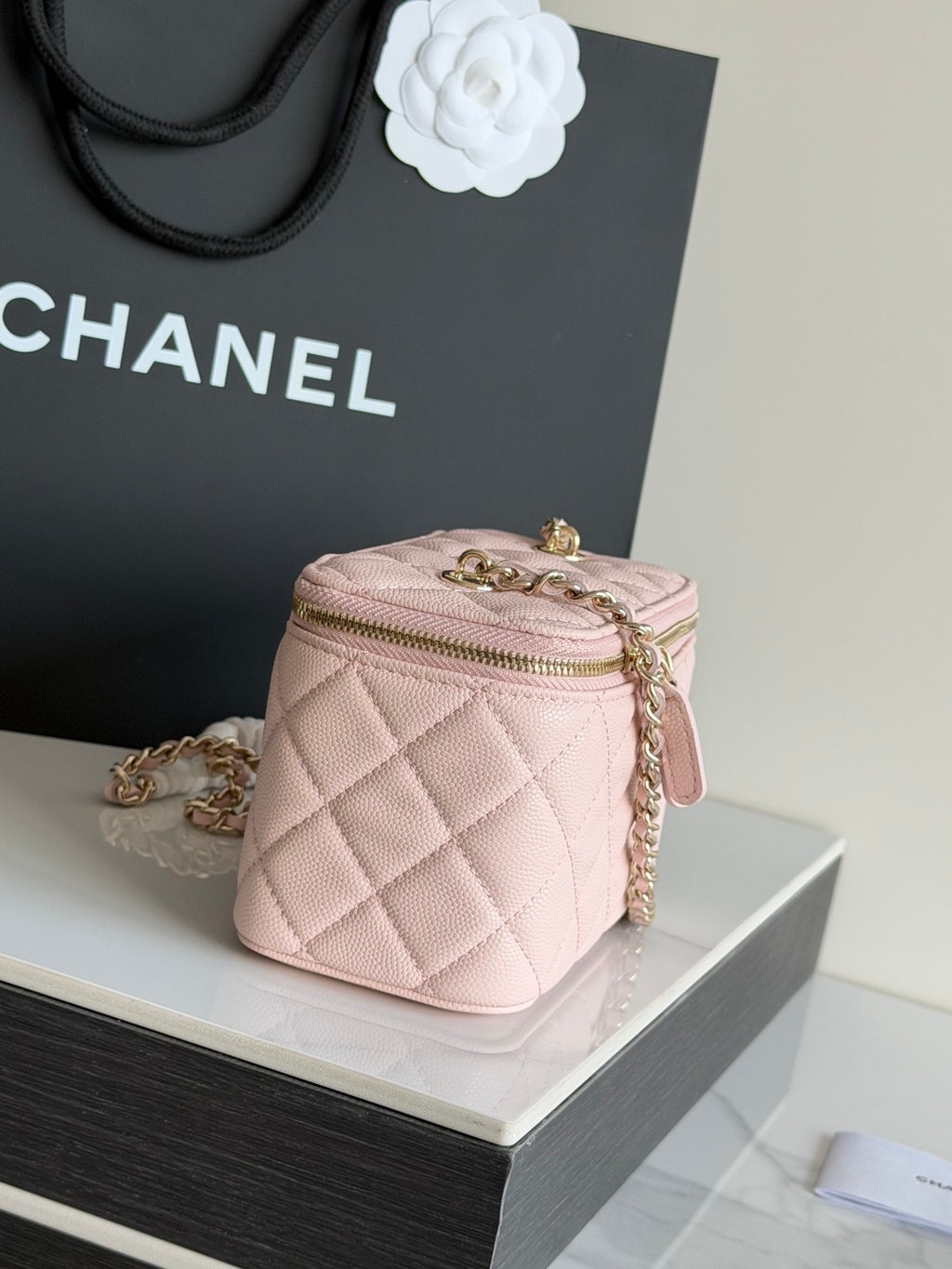 Pale pink quilted mini bag with gold-tone chain strap and top zipper.
