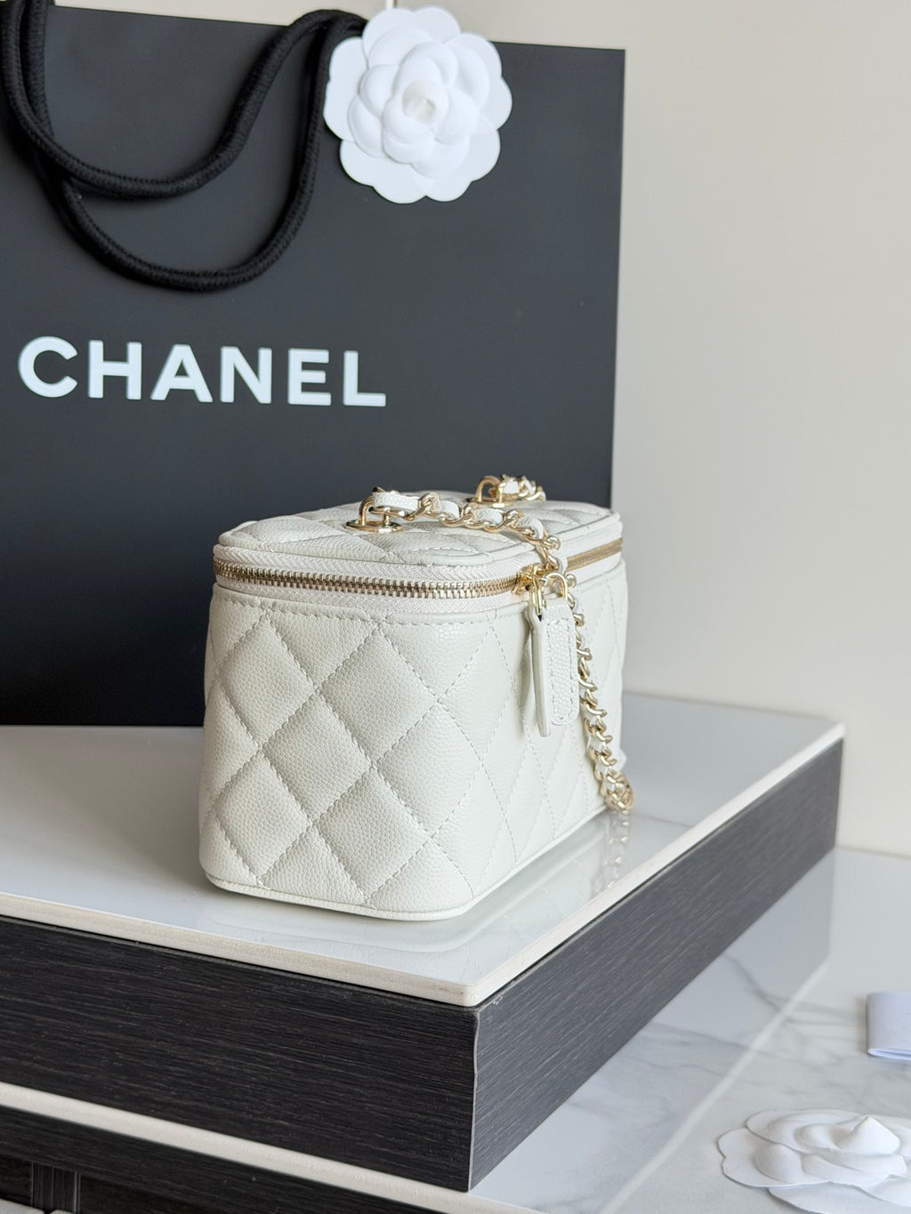 White quilted Chanel mini bag with gold clasp hardware, chain strap, and top zip