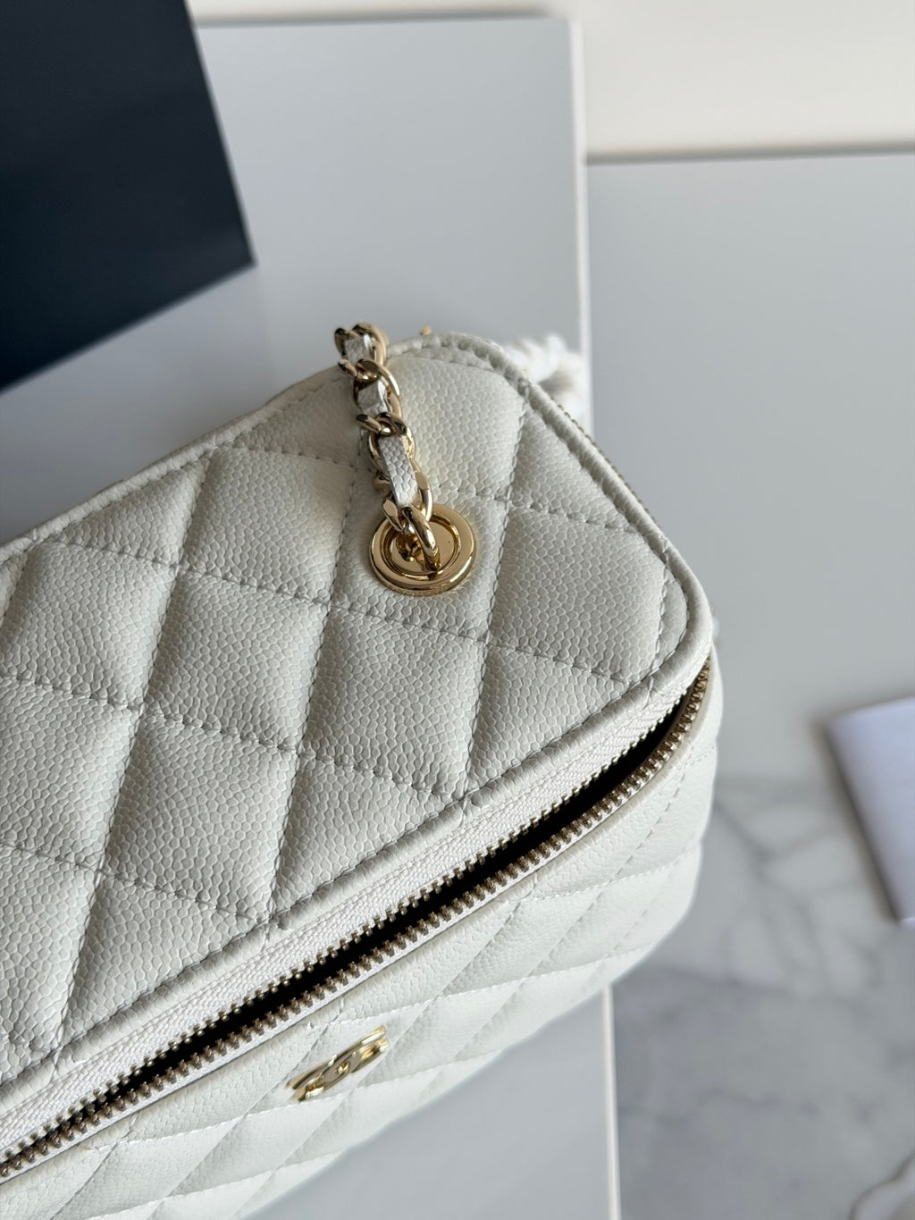 Chanel bag with quilted white leather, gold chain strap, and zip top close-up