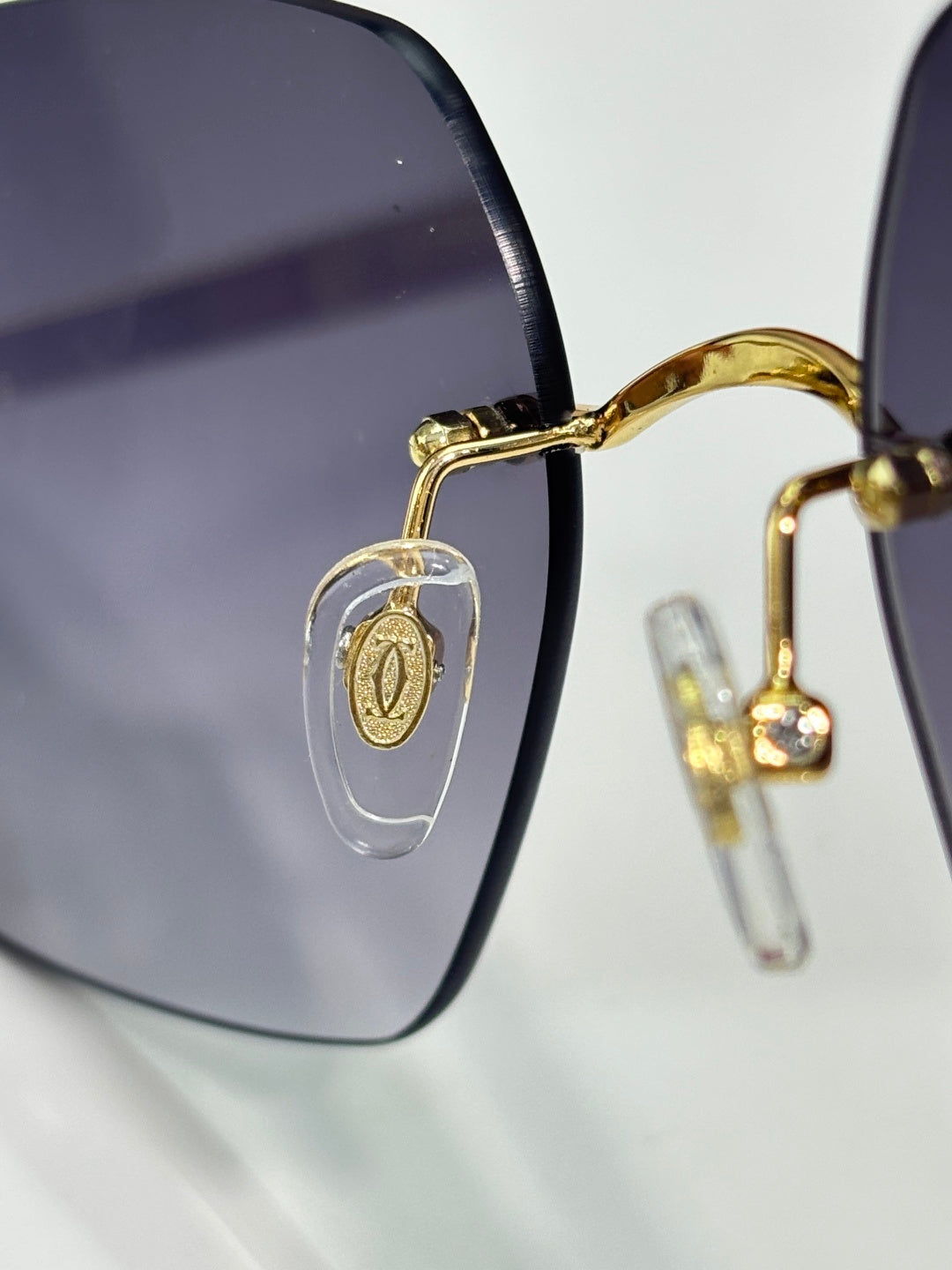 Sunglasses close-up: gold frame with dark lenses and oval emblem on lens arm