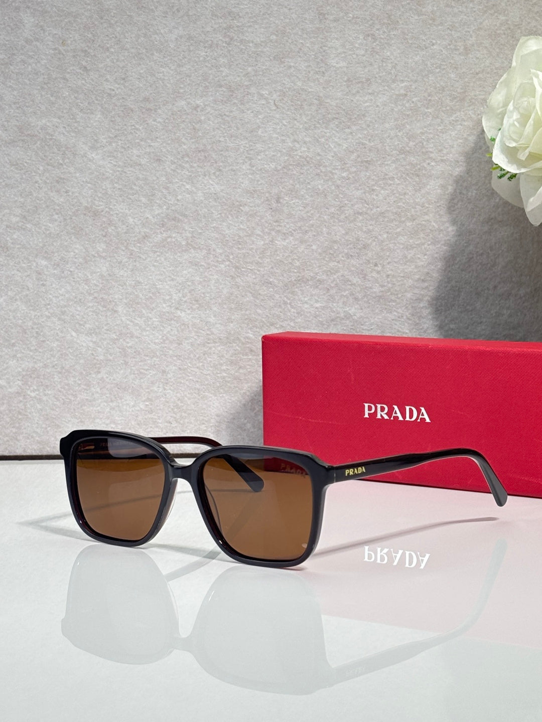 Black square sunglasses with brown-tinted lenses and Prada logo on temples