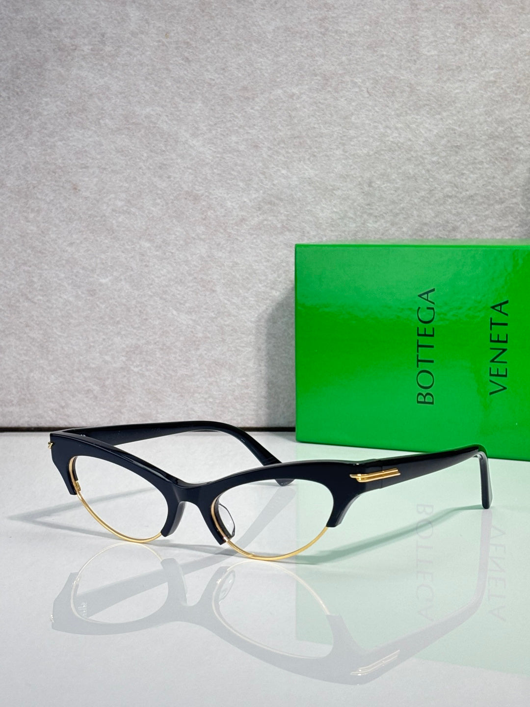 Bottega Veneta glasses with black frames, gold temple accents, and clear lenses