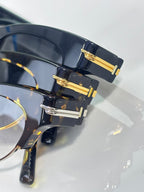 Eyeglasses close-up: dark acetate frame with gold hinge bars and tinted lenses.