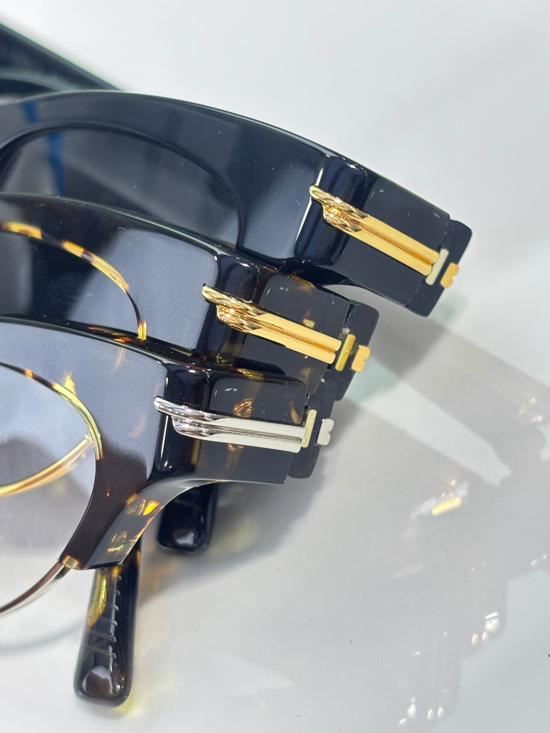 Eyeglasses close-up: dark acetate frame with gold hinge bars and tinted lenses.