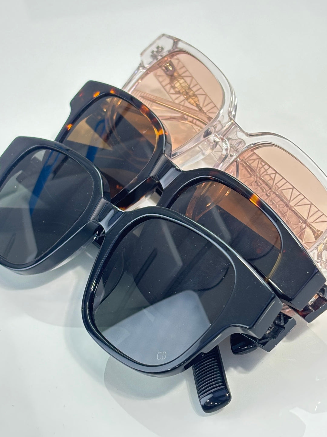 Stacked sunglasses: black, tortoiseshell, and clear frames with tinted lenses