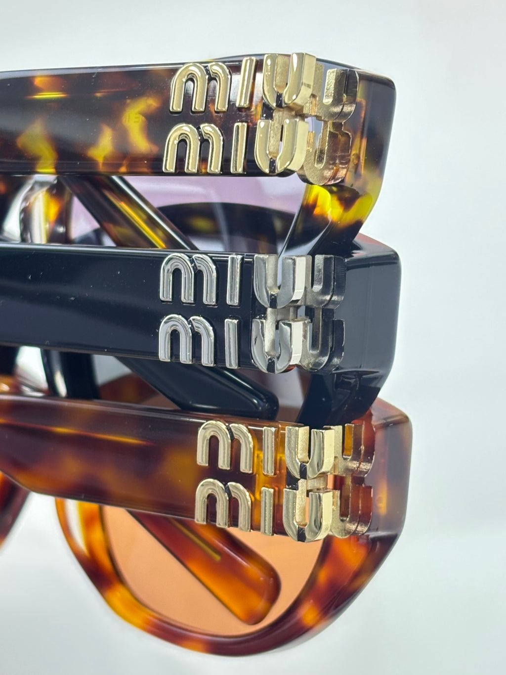 MiuMiu eyeglasses close-up of gold-tone logo temples over dark tortoiseshell frames