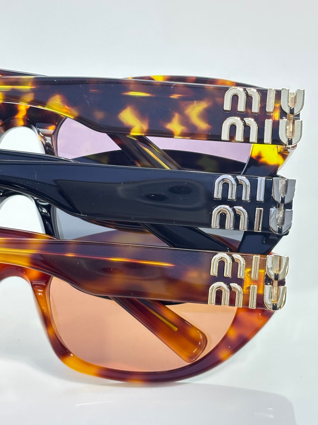 MiuMiu eyeglasses close-up of stacked frames and gold-tone logo hardware