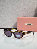 MiuMiu eyeglasses with tortoiseshell acetate frames and dark lenses, beside a pink case