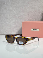 MiuMiu eyeglasses with tortoiseshell acetate frames and dark lenses, beside a pink case