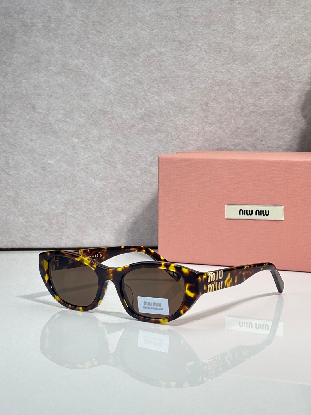 MiuMiu eyeglasses with tortoiseshell acetate frames and dark lenses, beside a pink case
