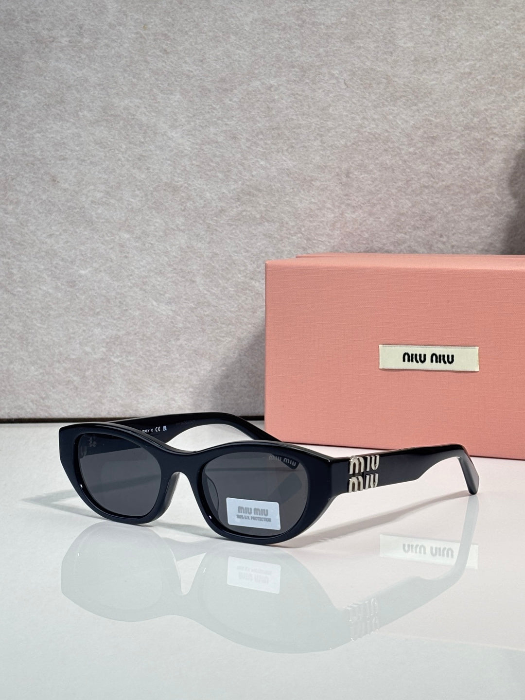 MiuMiu eyeglasses with dark acetate frames and black lenses, beside a pink case
