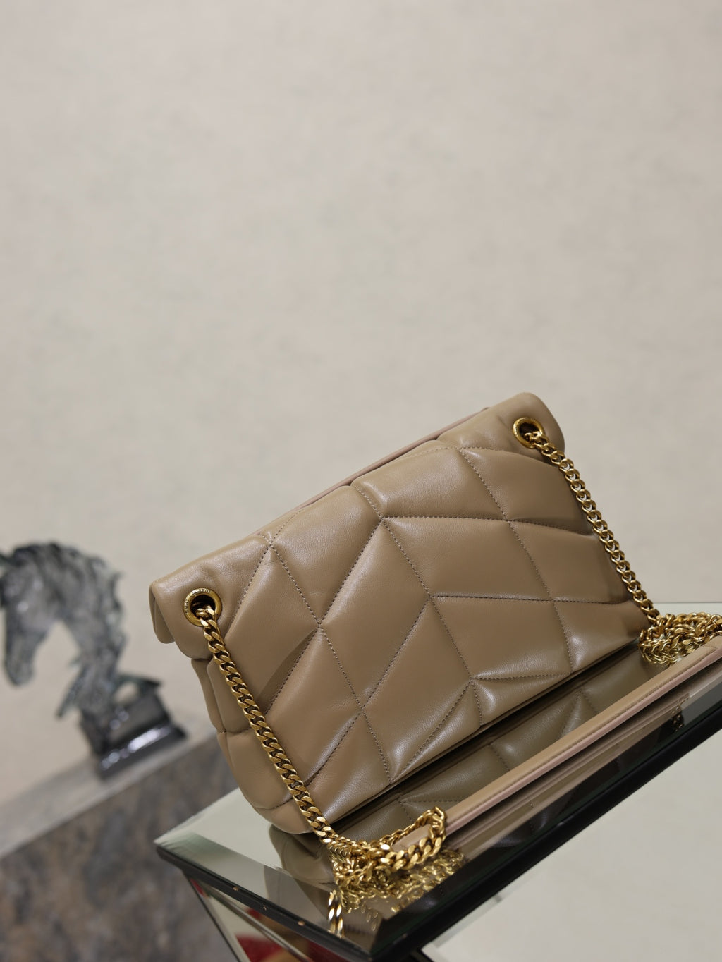 YSL quilted beige flap bag with gold chain strap on a display stand