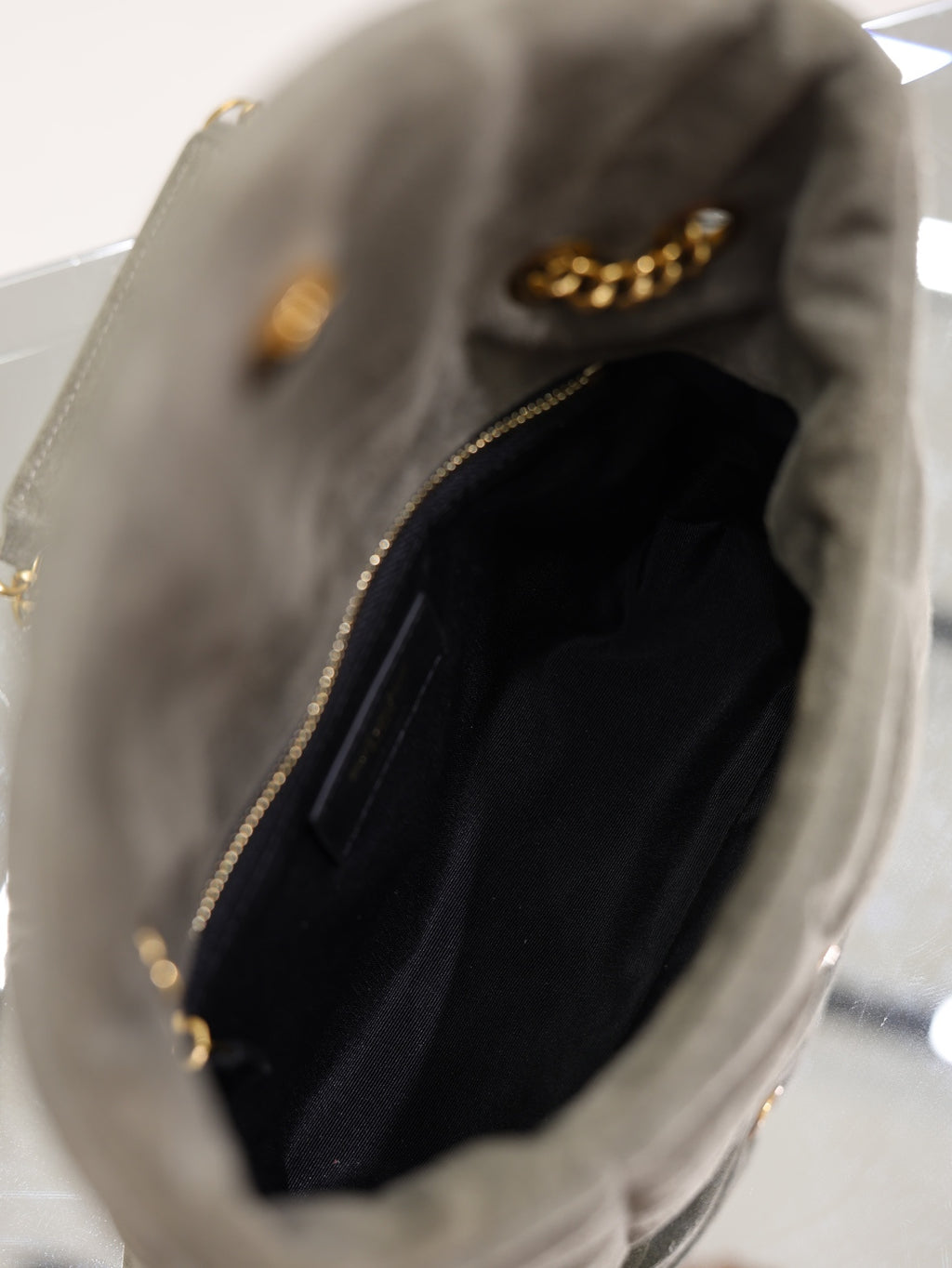 Gray suede shoulder bag with open top and black fabric lining, zipper edge