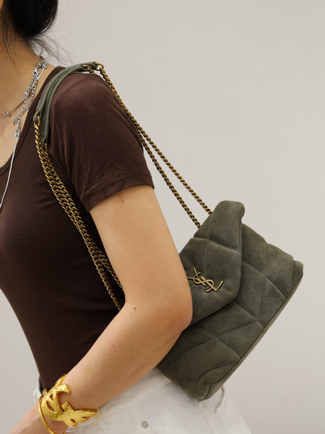 Gray quilted shoulder bag with gold YSL logo on flap and chain strap over arm