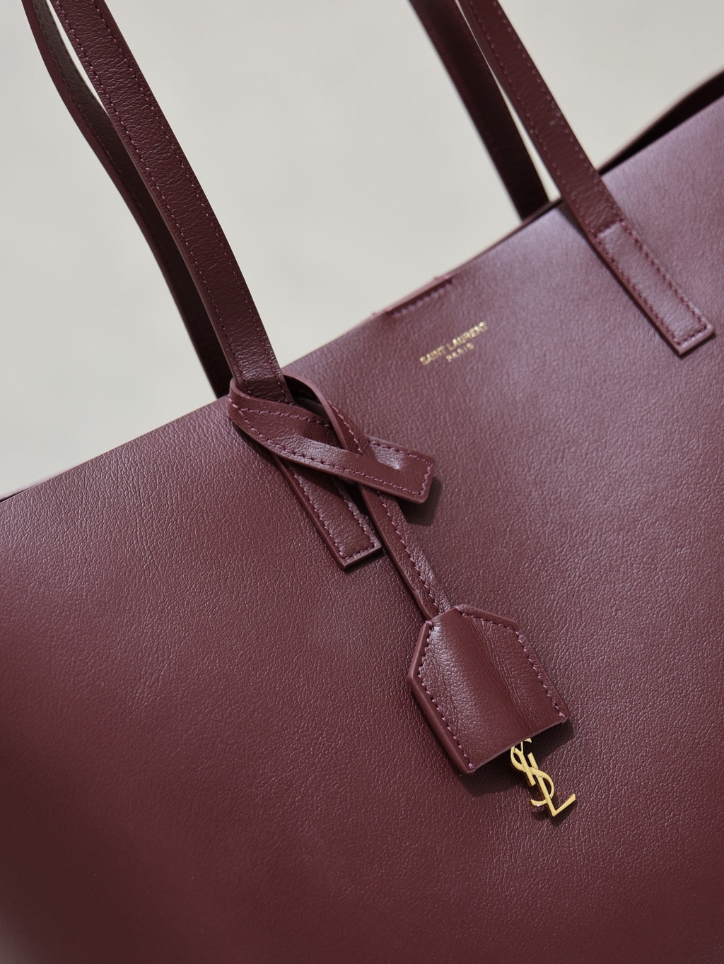 YSL burgundy leather tote bag close-up of front strap and gold-tone charm