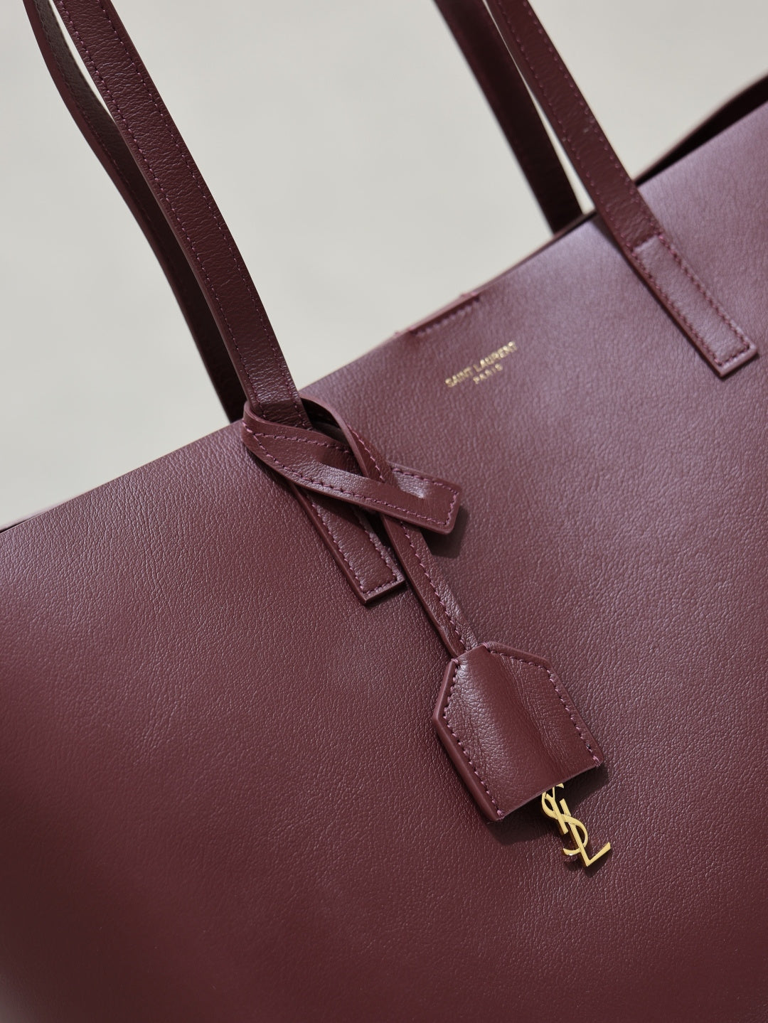 YSL burgundy leather tote bag close-up of front strap and gold-tone charm