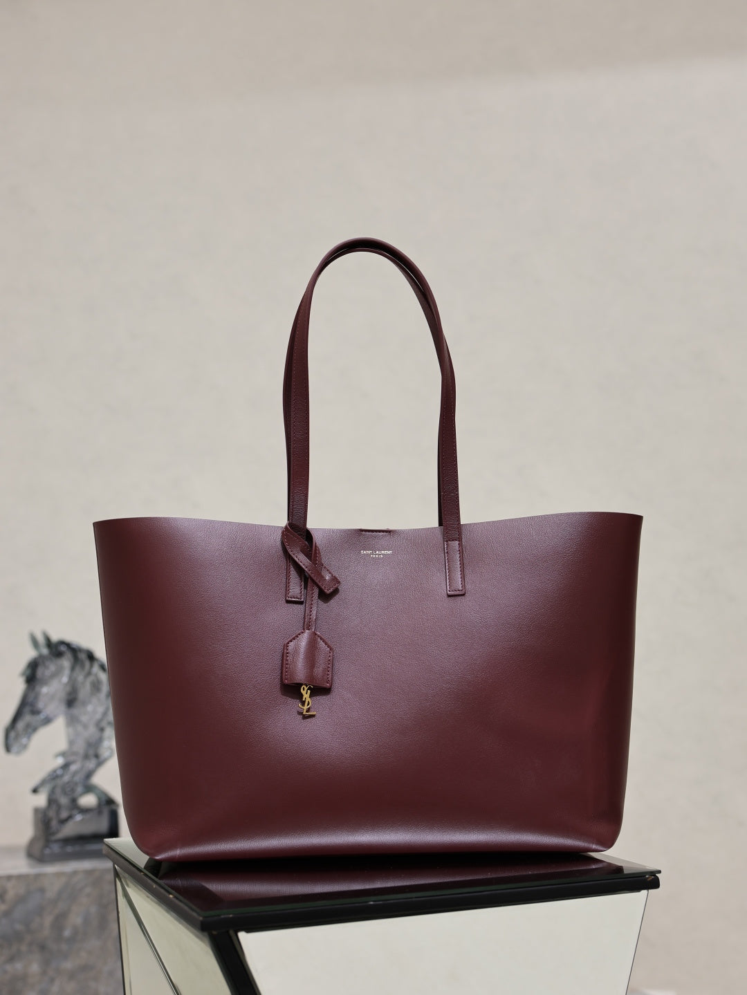 YSL burgundy tote bag with top handles and dangling gold-tone logo charm