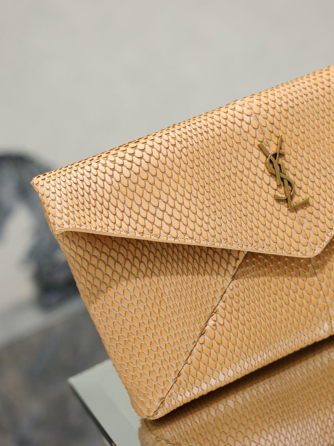 YSL envelope clutch bag close-up, textured tan flap with gold-tone YSL emblem