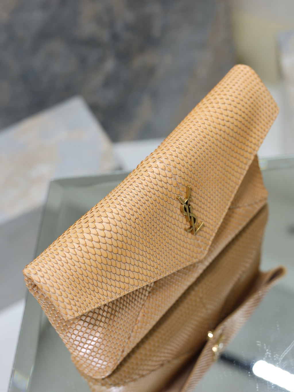 YSL envelope clutch bag angled view, textured tan with fold-over flap and logo