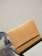 YSL envelope clutch bag top view, textured tan with folded flap and gold logo